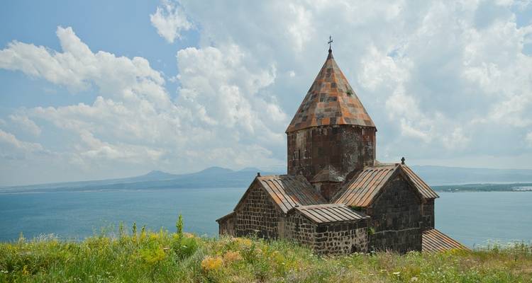 L'ancienne église en pierre de Sevanavank surplombant les eaux bleues du lac Sevan sous un ciel dégagé.