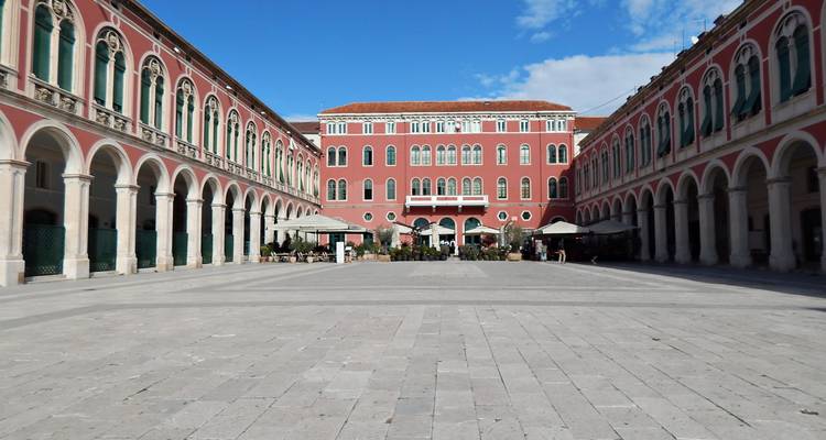 Plaza amplia enmarcada por arcadas rojo neoclásicas en la plaza Prokurative de Split