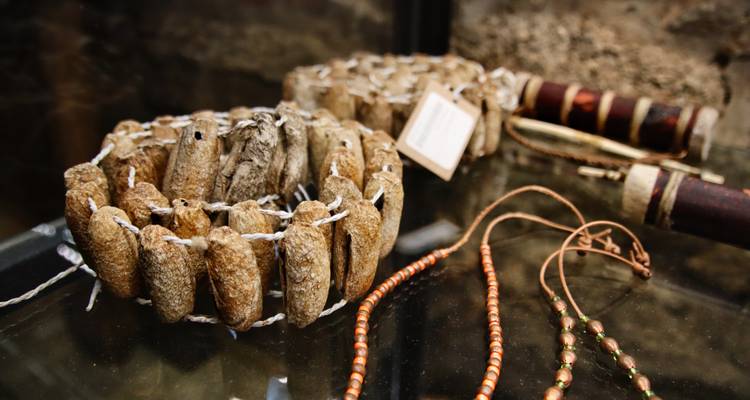 Display of traditional handcrafted items including dried fish bracelets and beaded necklaces in a museum.
