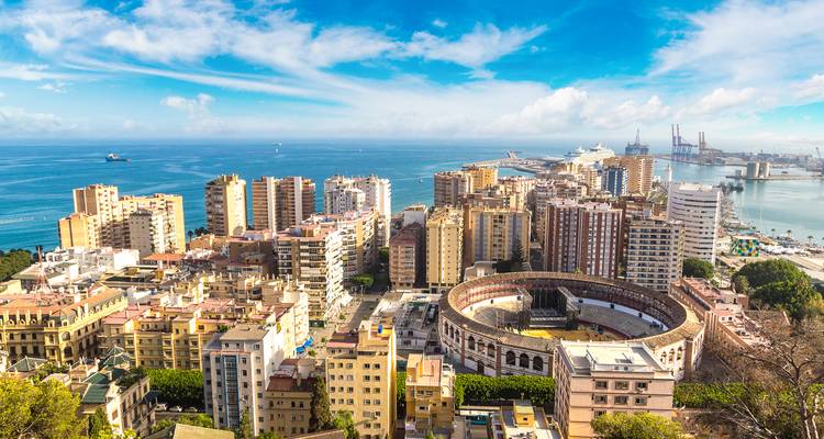 Hochgelegene Panoramabeschreibung des Hafens von Málaga mit Blick auf die Skyline mit Kreuzfahrtschiffen, Containerladekränen, die Stierkampfarena und das glitzernde blaue Meer.
