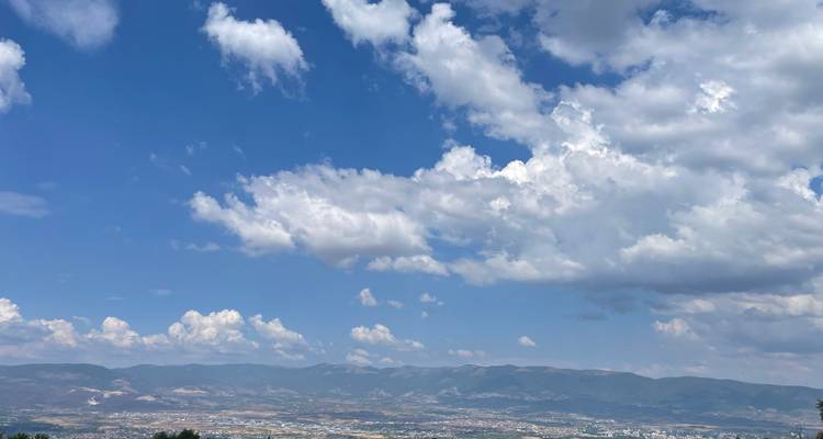 Amplio paisaje urbano en un valle bajo montañas ondulantes y un cielo con nubes blancas dispersas.