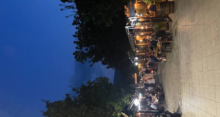 Callejón peatonal lleno de vida, bordeado de restaurantes y comedores al aire libre iluminados al anochecer.