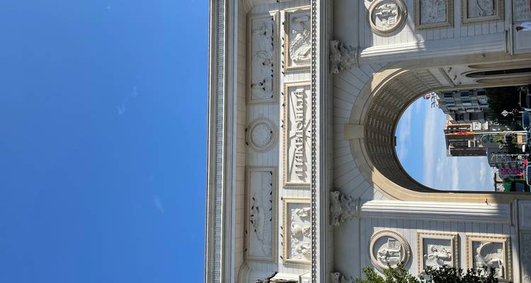 Arco triunfal de mármol blanco de pie contra un cielo azul brillante.