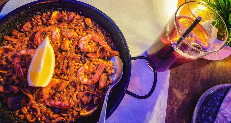 Paella de mariscos en una sartén con un vaso de sangría sobre una mesa de madera.