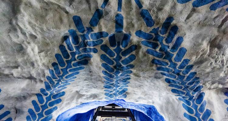 Paredes de caverna con patrón azul del techo de una estación de metro decorada con arte y escalera mecánica abajo.