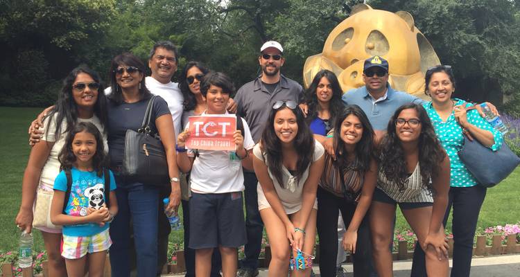 Un groupe de visite multigénérationnel souriant pose devant une grande sculpture en bronze ludique dans un parc urbain.