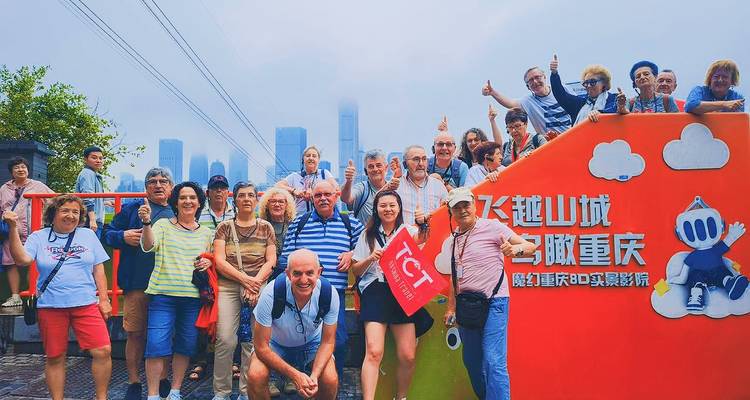 Un grand groupe de touristes posant devant un décor à thème orange de Chongqing avec la skyline de la ville moderne visible en arrière-plan brumeux.