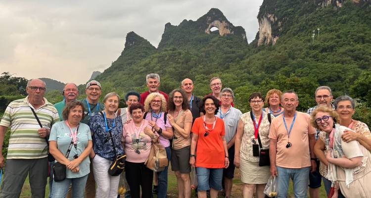 Groupe de visite souriante devant des montagnes de karst verdoyantes avec une ouverture en arche naturelle arrondie.