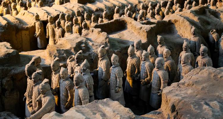Des rangées de Guerriers en Terre Cuite de taille nature se dressant à l'intérieur de la fosse excavée, éclairées par des lumières chaudes d'intérieur.
