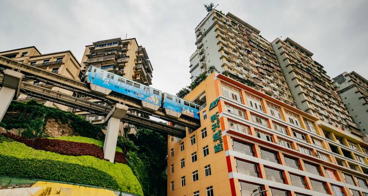 Le monorail bleu de Chongqing passe à travers des immeubles d'habitation de grande hauteur, photographié depuis le niveau de la rue.