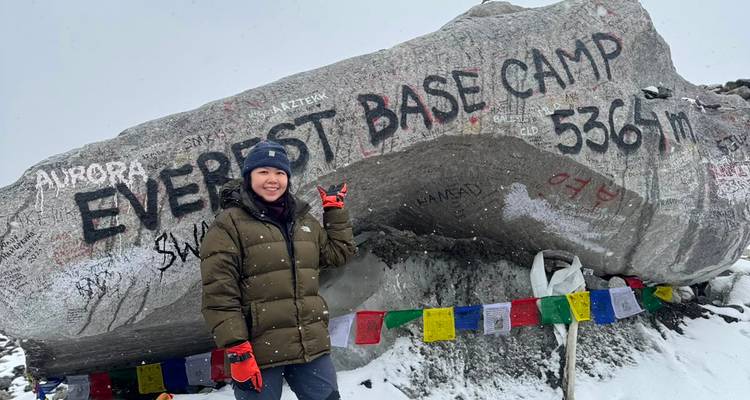 Trekista con equipo de invierno señala una roca con inscripción que marca la altitud del Campamento Base del Everest