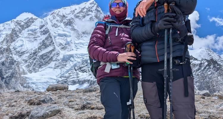 Dos alpinistas con equipo para clima frío se encuentran frente a un imponente pico himalayo cubierto de nieve