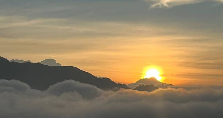 El sol dorado se asoma sobre un mar de nubes que rueda sobre las montañas distantes