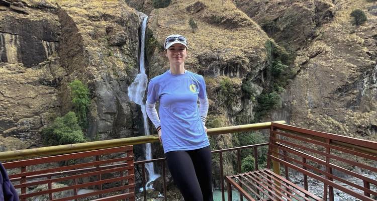 Un viajero posa en un balcón de madera con vistas a una cascada alta y un cañón escarpado