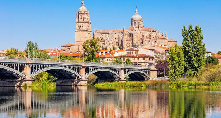 Riverside view of Salamanca Cathedral rising above a historic iron bridge reflected in calm water