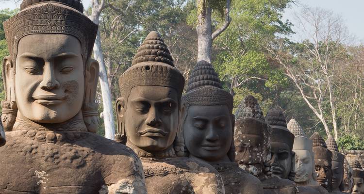 Row of massive stone guardian heads lining the causeway to Angkor Thom amid jungle greenery.