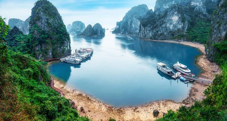 Panoramic aerial view of a secluded bay in Halong featuring heart-shaped water framed by green cliffs and boats.