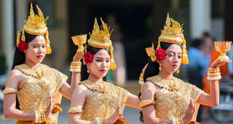 Three Cambodian dancers in golden traditional attire performing an Apsara dance outdoors.