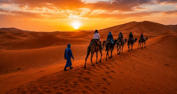 Caravane de touristes chevauchant des chameaux le long d'une crête de dune orange incandescente au coucher du soleil dans le Sahara.