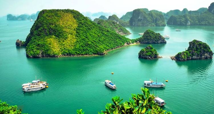 Les eaux turquoise de la baie d'Halong parsemées d'îles calcaires et de bateaux de tourisme naviguant entre elles.