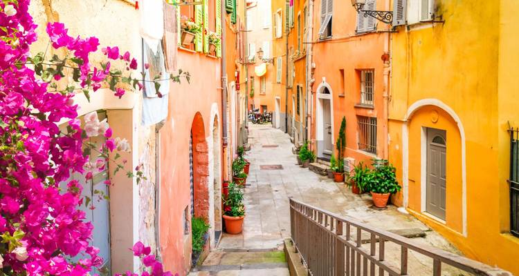 Charmante ruelle étroite bordée de maisons aux couleurs pastel, de plantes en pot et de fleurs de bougainvillée.
