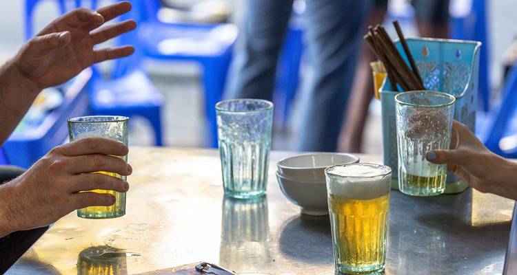 Primer plano de manos sosteniendo vasos de cerveza vietnamita fresca en mesas bajas de la calle