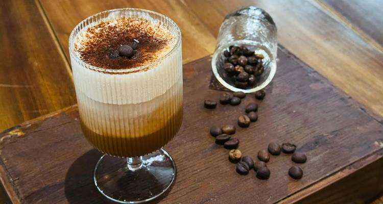 Vaso de cremoso café vietnamita con huevo coronado con cacao al lado de granos de café dispersos
