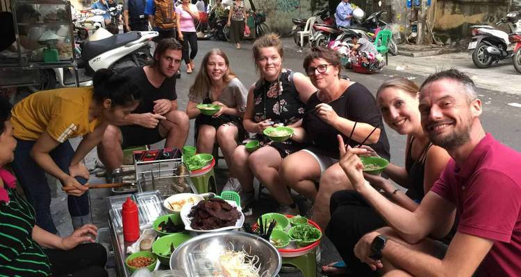 Los turistas sentados en banquetas bajas disfrutan de comida callejera de un vendedor de barbacoa en la acera