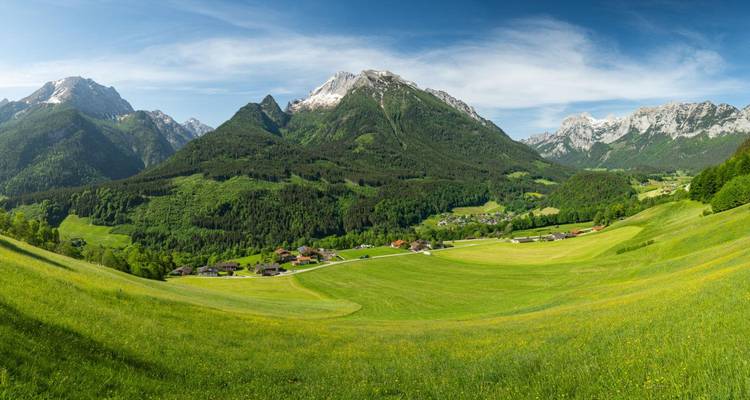 Een breed panorama van groene rollende weiden omlijst door Oostenrijks sneeuwtoppen van de Alpen onder een blauwe hemel.