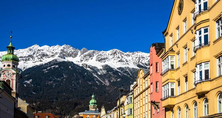 Kleurrijke panden in Innsbruck tegen sneeuwbedekte alpiene pieken onder een kristalhelder blauwe hemel.