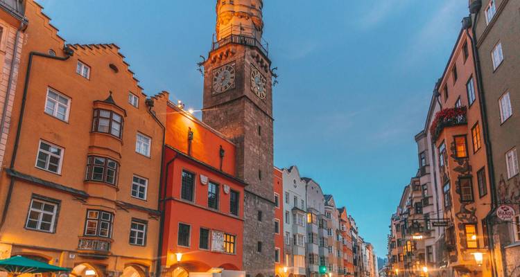 Los coloridos edificios medievales y una torre de reloj de piedra brillan bajo la cálida luz del atardecer en una calle de Innsbruck.