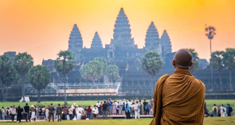 Un moine en robe contemple les tours d'Angkor Wat au lever du soleil tandis que des foules se rassemblent sur la pelouse.