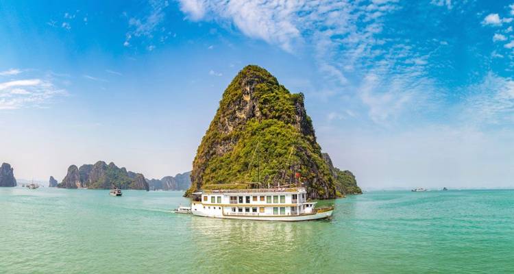 Un bateau de croisière blanc navigue devant les imposants pics rocheux en calcaire dans les eaux turquoise de la baie d'Ha Long.