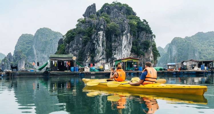 Deux voyageurs pagaient dans un kayak jaune sur une eau émeraude calme, entourée de falaises calcaires spectaculaires.
