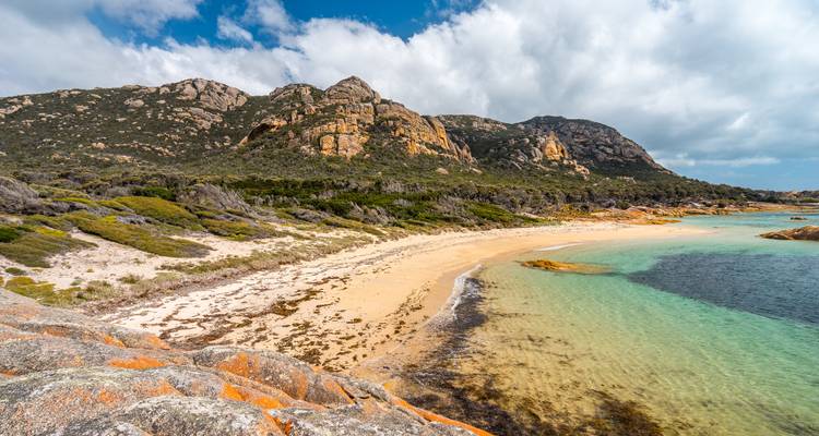 Playa en forma de media luna apartada con agua azul turquesa cristalina respaldada por cerros de granito escarpado y maleza.