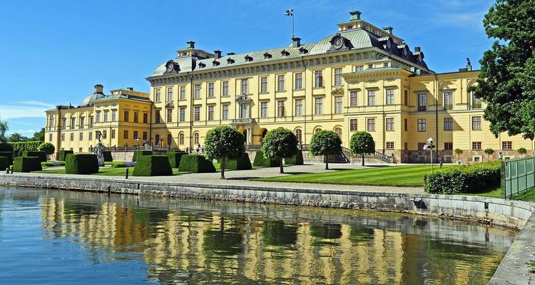 El elegante Palacio Drottningholm amarillo reflejado en aguas tranquilas bajo un cielo azul de verano.