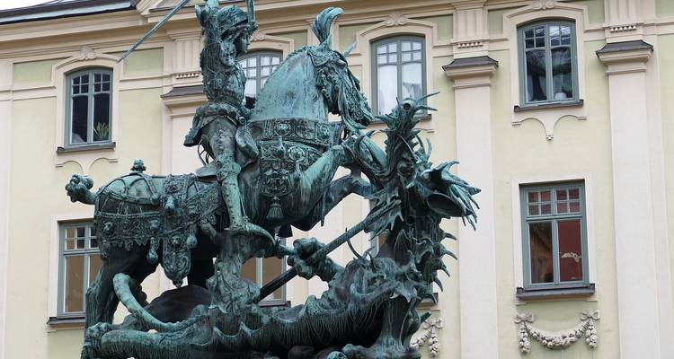 Estatua de bronce de San Jorge matando al dragón sobre la fachada de un edificio en tonos pastel en Estocolmo.