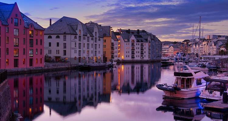 Vista serena del atardecer con edificios coloridos en el paseo marítimo y barcos amarrados reflejándose en el canal de Ålesund.