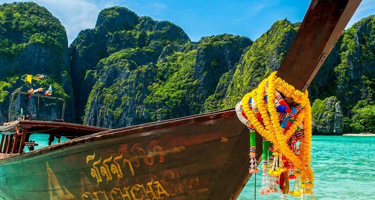 Un bateau à longue queue thaïlandais traditionnel, décoré de guirlandes de fleurs, flotte sur une eau turquoise devant des falaises calcaires spectaculaires.