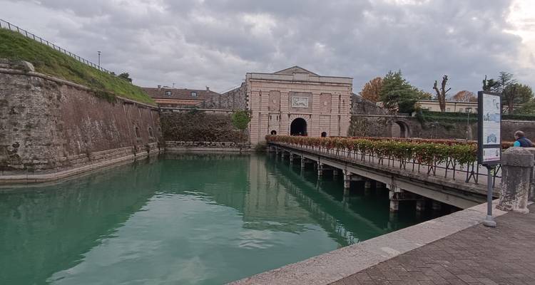 Puerta de piedra histórica y foso de color turquesa de la fortaleza de Peschiera del Garda bajo un cielo nublado