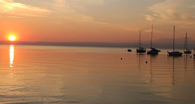 Lago de Garda tranquilo al atardecer con veleros amarrados en aguas tranquilas teñidas de naranja