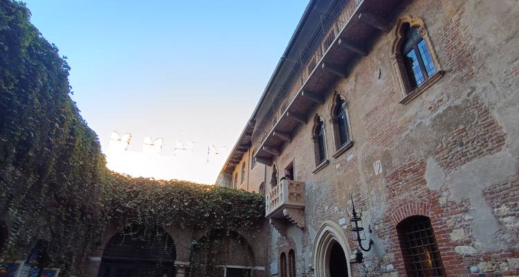 El patio de la Casa de Julieta en Verona con paredes cubiertas de hiedra y el famoso balcón