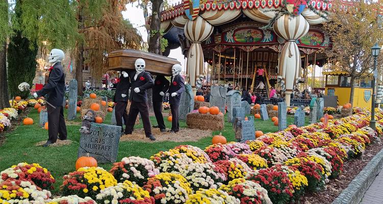 Exhibición de Halloween con esqueletos cargadores de ataúd y coloridas macetas de flores junto a un carrusel vintage