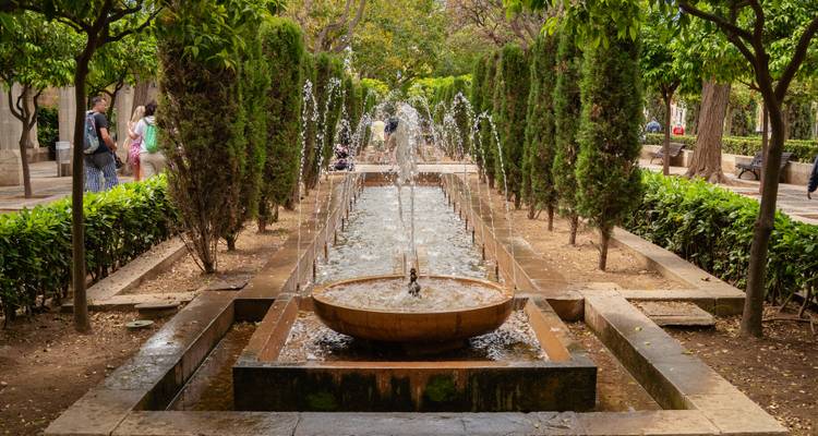 Allée de jardin longue avec jets de fontaine centrale flanqués d'arbres de cyprès élancés