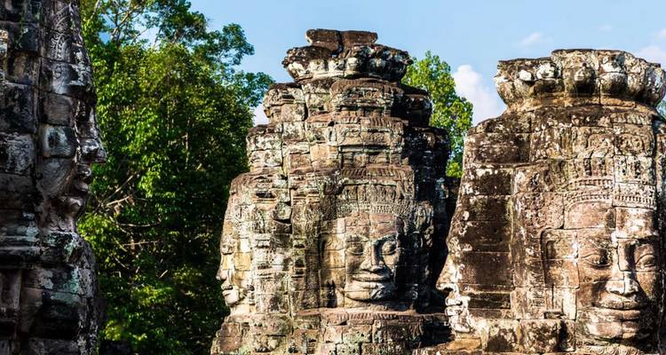 Gros plan des visages géants sculptés dans la pierre sur les tours des temples d'Angkor entourées par la jungle.