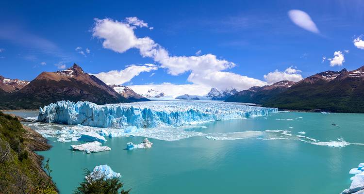 Massive Wand des Perito-Moreno-Gletschers, die auf türkisfarbene Gewässer inmitten von patagonischen Gipfeln und blauem Himmel trifft.