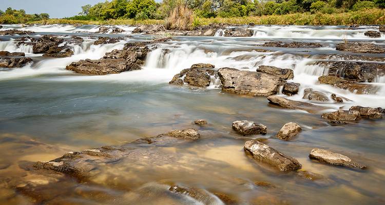 Mehrere felsige Wasserfälle erzeugen seidig wirkende Wasserflüsse über ein breites Flussbett.