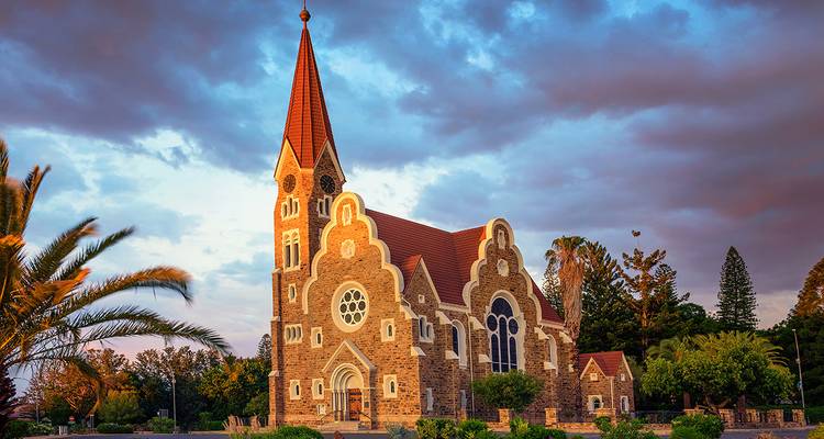 Die rotgedeckte Christuskirche in Windhoek leuchtet bei Sonnenuntergang gegen dramatische Wolken.