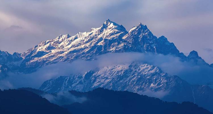 Le massif enneigé du Kangchenjunga perçant les nuages au-dessus des contreforts himalayens vallonnés.