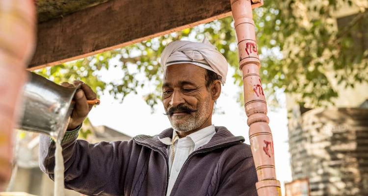 Vendeur de chai indien souriant en turban versant du thé à un étal de rue.